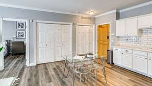 Una cocina moderna con armarios blancos, una mesa de comedor de vidrio y piso de madera.