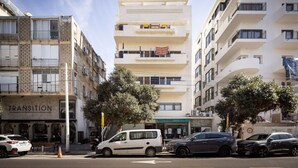 Un edificio de varios pisos con balcones, un escaparate visible con el nombre 'TRANSITION' en la planta baja y una tienda 'Just Print' en el segundo piso.