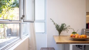 Una cocina con encimera de madera, un cuenco de fruta, una planta en maceta y un ventanal con vistas al verdor exterior.