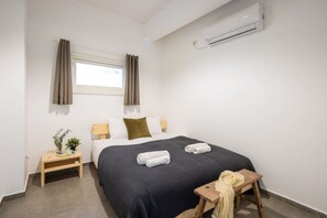 A hotel room with a bed, a bedside table, an air conditioning unit, and a window with curtains. - Old North 2BR | Private Garden by SeaNRent (Tel Aviv-Yafo)