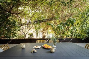 Un área de comedor al aire libre con una mesa lista para dos personas, rodeada de abundante vegetación.