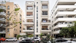 Un edificio residencial de varios pisos con balcones, una estructura vertical central y un estacionamiento con automóviles.