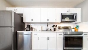 A modern kitchen with white cabinets, a stainless steel refrigerator, a microwave, a coffee maker, and an oven.