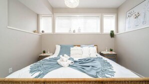 A bedroom with a bed, bedside tables, a hanging plant, and a window with blinds.