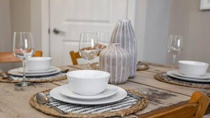 A dining table set with white plates, bowls, and wine glasses, accompanied by a patterned vase and woven placemats.