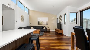 Un salon moderne avec un plancher en bois, un comptoir de bar blanc, un canapé noir et un téléviseur.