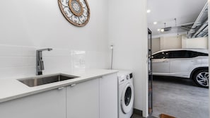 A modern kitchen with a stainless steel sink, white cabinets, and a washing machine. - Best of Both Worlds Inverloch (Inverloch)