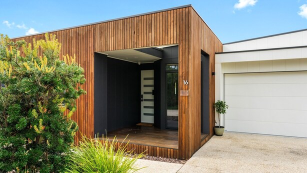 Une maison moderne avec une façade en bois, un portail de garage et un jardin bien entretenu.