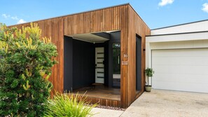 A modern house with a wooden exterior, a garage door, and a well-maintained garden. - Best of Both Worlds Inverloch (Inverloch)