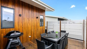 Une terrasse en bois avec un barbecue, une table et des chaises, et une clôture blanche.