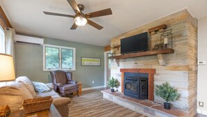 A living room with a stone fireplace, a television mounted above it, and a ceiling fan. - Laurel Highlands Getaway Chalet - Fire Pit, Game Room, Near Lake & Ski Resorts (Rockwood)