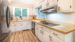 A modern kitchen with white cabinets, a stainless steel refrigerator, a wooden countertop, and a window providing a view of the outdoors. - Laurel Highlands Getaway Chalet - Fire Pit, Game Room, Near Lake & Ski Resorts (Rockwood)