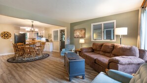 A spacious living room with a brown sofa, a blue armchair, and a dining area with wooden chairs and a table. - Laurel Highlands Getaway Chalet - Fire Pit, Game Room, Near Lake & Ski Resorts (Rockwood)