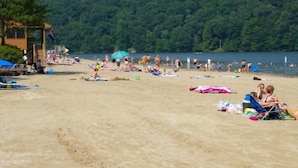 A beach with people sunbathing and swimming, surrounded by a forested hillside. - Laurel Highlands Getaway Chalet - Fire Pit, Game Room, Near Lake & Ski Resorts (Rockwood)