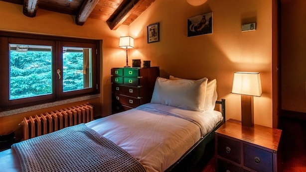 A bedroom with a bed, bedside lamps, a dresser, and a window with a view of greenery. - Villa Oasi - My Home in Como (Canzo)