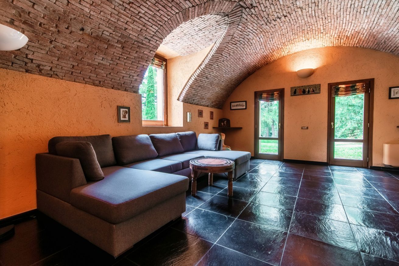Una stanza spaziosa con soffitto in mattoni, un divano componibile, un tavolino rotondo e ampie finestre.