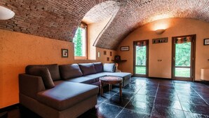 A spacious room with a brick ceiling, a sectional sofa, a round coffee table, and large windows. - Villa Oasi - My Home in Como (Canzo)