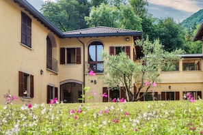 A two-story building with a balcony, a large arched window, and a door with a metal gate. - Villa Oasi - My Home in Como (Canzo)