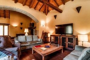 A cozy living room with a wooden ceiling, a television, a coffee table with books, and a fireplace. - Villa Oasi - My Home in Como (Canzo)
