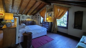 Une chambre à coucher avec un plafond en bois, un lit, une commode, une table de chevet, une lampe et une fenêtre avec des rideaux.
