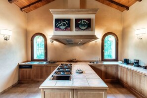 A kitchen with wooden cabinets, a central island, a stove, and two windows with arched tops. - Villa Oasi - My Home in Como (Canzo)