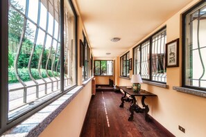 A hallway with large windows, a bench, and a table with a lamp. - Villa Oasi - My Home in Como (Canzo)