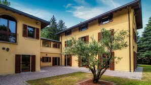 Un bâtiment à deux étages avec une cour intérieure, des volets en bois et un arbre.