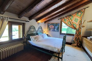 A bedroom with a bed, a radiator, a window with curtains, a painting on the wall, and a wooden ceiling. - Villa Oasi - My Home in Como (Canzo)