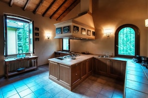 A spacious kitchen with a large island, wooden cabinets, and a view of the outdoors through large windows.