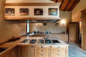 A kitchen with a large island, wooden cabinets, and a high ceiling with exposed beams. - Villa Oasi - My Home in Como (Canzo)