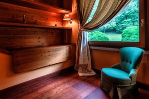 Un intérieur en bois avec un banc, un fauteuil de couleur turquoise, une fenêtre avec des rideaux et une lampe fixée au mur.