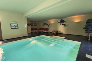 An indoor swimming pool with steps leading into it, a red sofa, and wall-mounted fish decorations. - Villa Oasi - My Home in Como (Canzo)