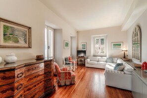 A spacious living room with a wooden floor, a white sofa, a striped armchair, and a TV. - Villa Vica - My Home in Como (Musso)