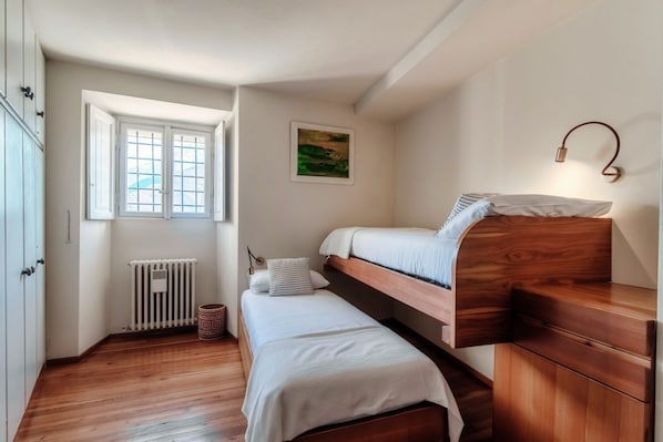 A bedroom with a bunk bed, a radiator, a window, and a wall-mounted light fixture.