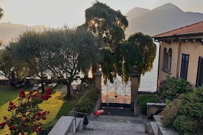 A courtyard with a staircase leading to a building, surrounded by trees and a view of a body of water.