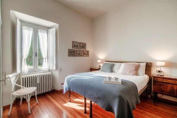 Un dormitorio con cama, una silla, un radiador y una ventana con cortinas.