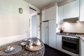 A modern kitchen with white cabinets, a granite countertop, a built-in oven, and a stainless steel range hood.