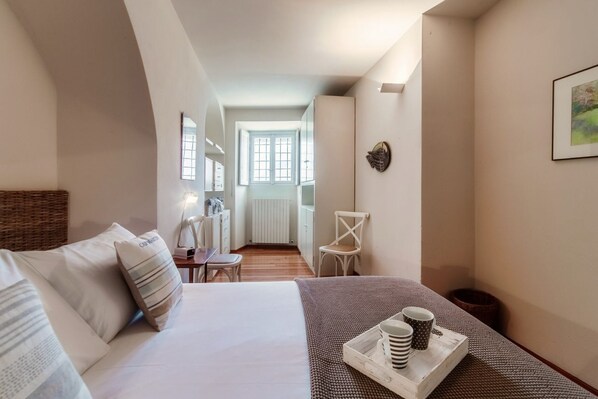 A bedroom with a bed, a desk, a chair, a tray with cups, and a window.