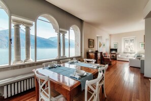 Un comedor con vistas a un lago, piso de madera y muebles blancos.