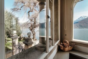 A room with a large window overlooking a lake and mountains, a stone balustrade, and a wicker basket on the windowsill.