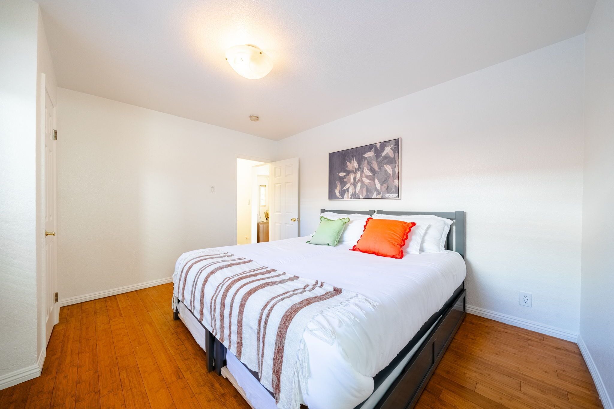 Een slaapkamer met een bed, een schilderij en een deur naar een andere kamer.