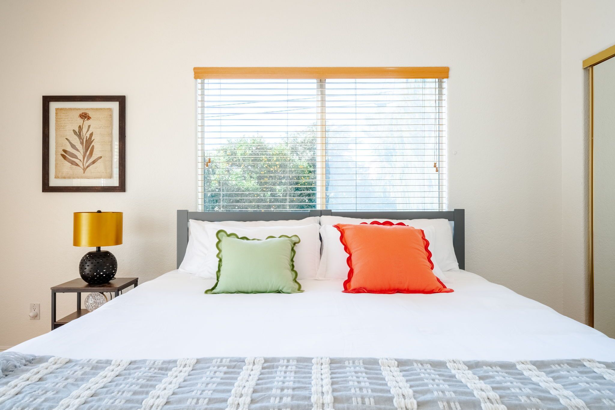 A neatly made bed with white bedding and two pillows, a bedside lamp, and a framed artwork on the wall.