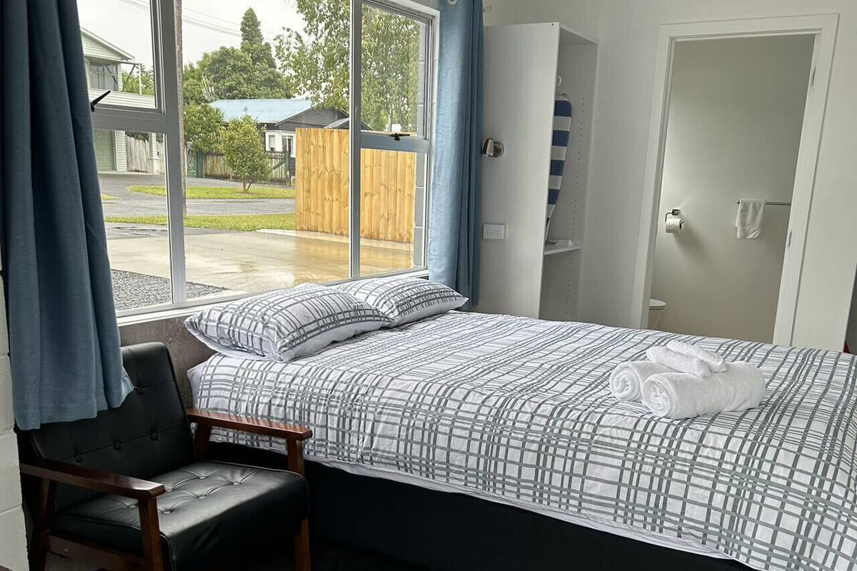 A bedroom with a bed, a chair, a wardrobe, and a window with curtains.