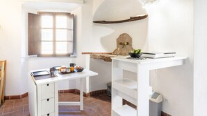 A small kitchen with a white countertop, a window with blinds, a wooden beam on the ceiling, and a sink with a faucet.