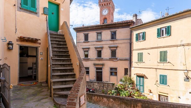 A narrow street with a staircase leading to a building with a clock tower.
