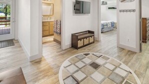 Ett modernt hotellrum med trägolv, en rund matta, en tv som är monterad på väggen och en skylt med texten ”Välkommen”.