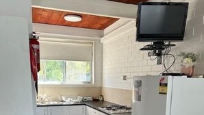 Une cuisine compacte avec des meubles blancs, un four à micro-ondes encastré, une cuisinière et un téléviseur fixé au-dessus du plan de travail.