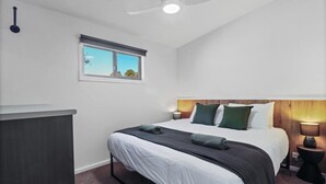 Ein Schlafzimmer mit Bett, Nachttisch, Schreibtisch, Fenster und Deckenventilator.