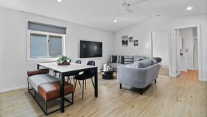 Ein modernes Wohnzimmer mit Essbereich, einem grauen Sofa, einem Flachbildfernseher und einem Deckenventilator.