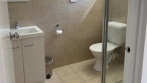 A bathroom with beige tiles, a white sink, a toilet, and a glass shower enclosure.